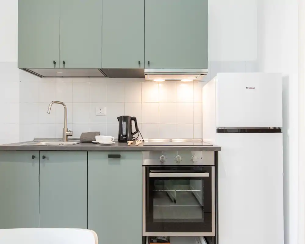 Cucina moderna compatta con ante verde menta, forno incassato, piano cottura e frigorifero a colonna: ben illuminata e ordinata, ideale per un annuncio.