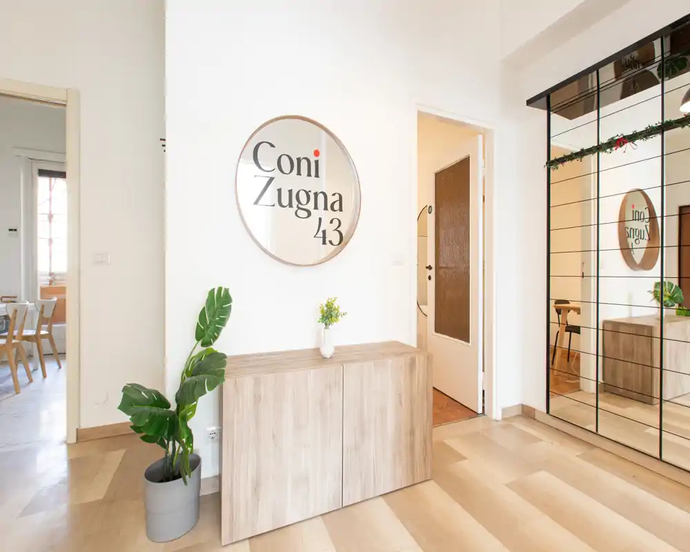 Ingresso luminoso e accogliente con mobile consolle in legno, specchio rotondo decorativo e ampia armadiatura a specchio che dona profondità e spazio.