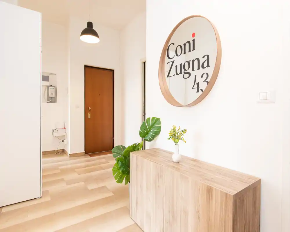 Ingresso luminoso e minimal con una consolle in legno, specchio rotondo e pianta decorativa — stile moderno e pavimento in legno caldo.