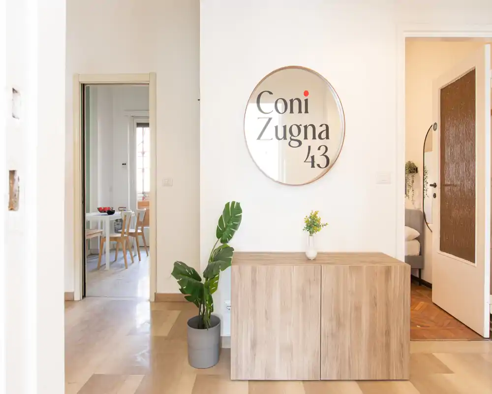 Ingresso luminoso e accogliente con consolle in legno, specchio rotondo decorativo e pianta in vaso; toni neutri e luce naturale che conduce alle stanze adiacenti.