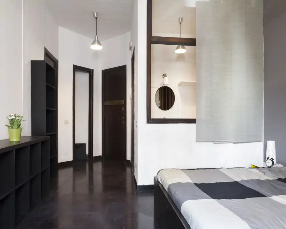 Dormitorio luminoso y moderno con cama bien hecha en primer plano, estantes sencillos y estética limpia y minimalista.