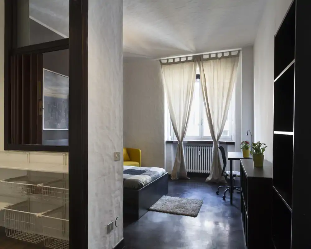 Dormitorio moderno y luminoso con cama baja, alfombra y escritorio junto a la ventana que deja pasar luz natural difusa.