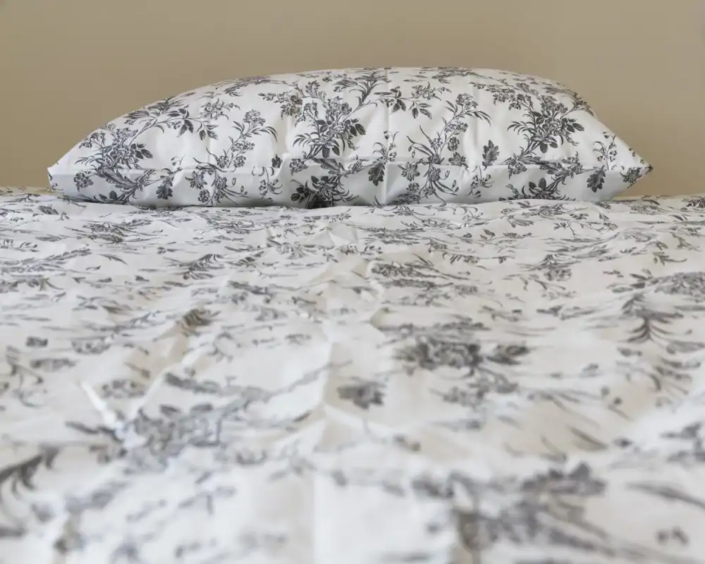 Primo piano di un letto ben rifatto con lenzuola stampate e cuscino coordinato, fotografato con luce morbida e uniforme—ottimo per evidenziare i dettagli della biancheria.