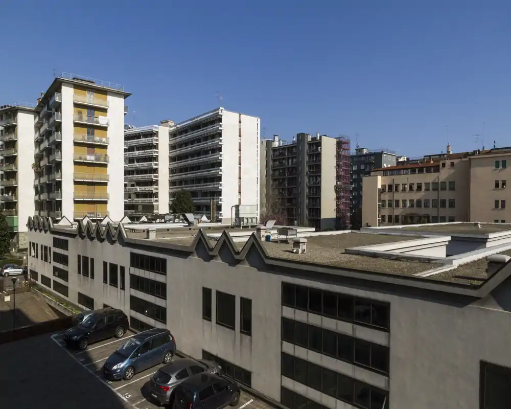 Vista esterna della città con tetti, auto parcheggiate e condomini circostanti sotto un cielo sereno — adatta a illustrare una vista esterna o il panorama da un balcone.