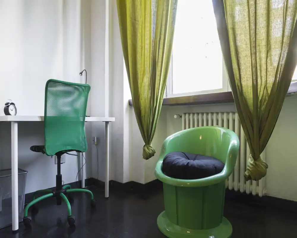 Angolo giorno/lavoro compatto con poltrona verde e sedia da scrivania coordinate vicino a una finestra luminosa; stile moderno e luce naturale.