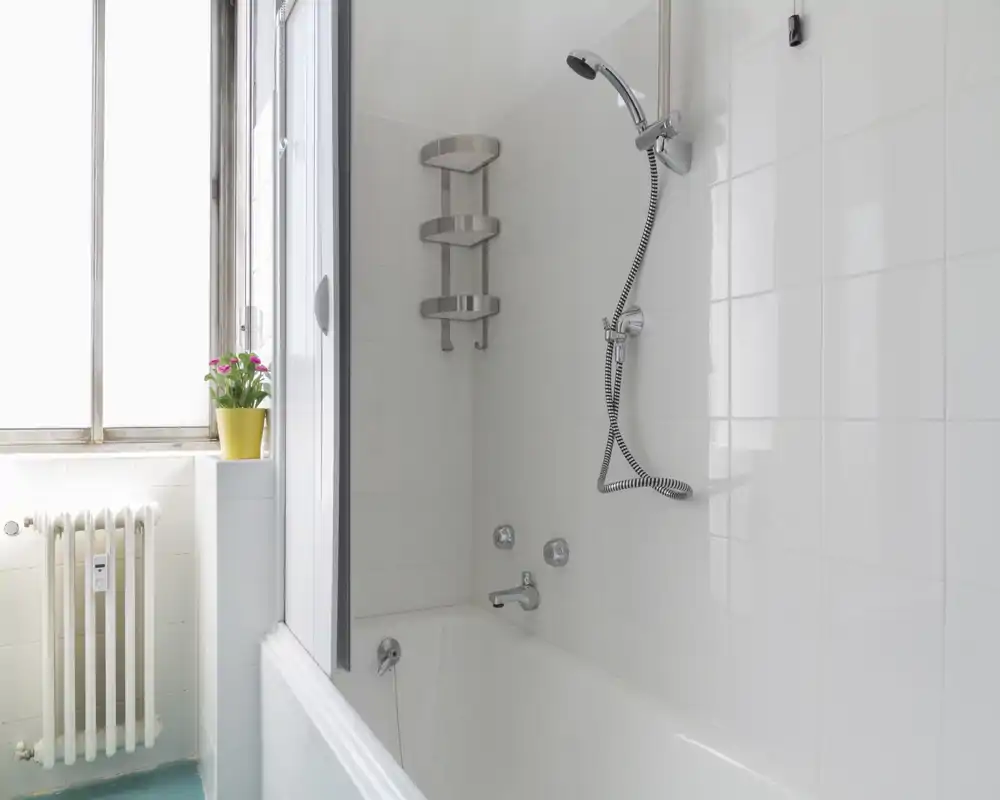 Bagno pulito e luminoso con vasca, doccia a muro e pareti piastrellate; un piccolo vaso di fiori sul davanzale aggiunge un tocco gradevole.