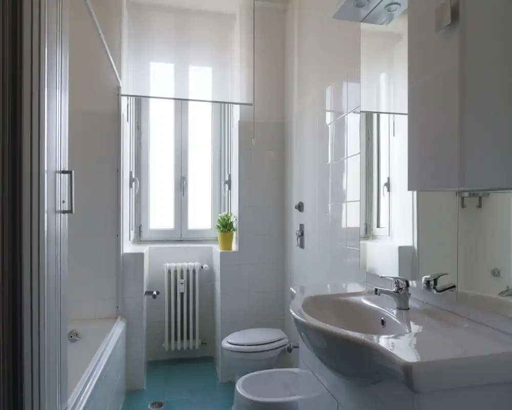 Bagno luminoso e pulito con lavabo, WC, bidet, vasca e ampia finestra che lascia entrare luce naturale; piastrelle e sanitari moderni e semplici.