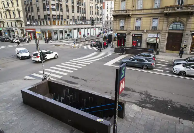 Urban street view showing a metro entrance and a pedestrian crossing; cars and buildings frame the scene, suitable to illustrate city transport access.