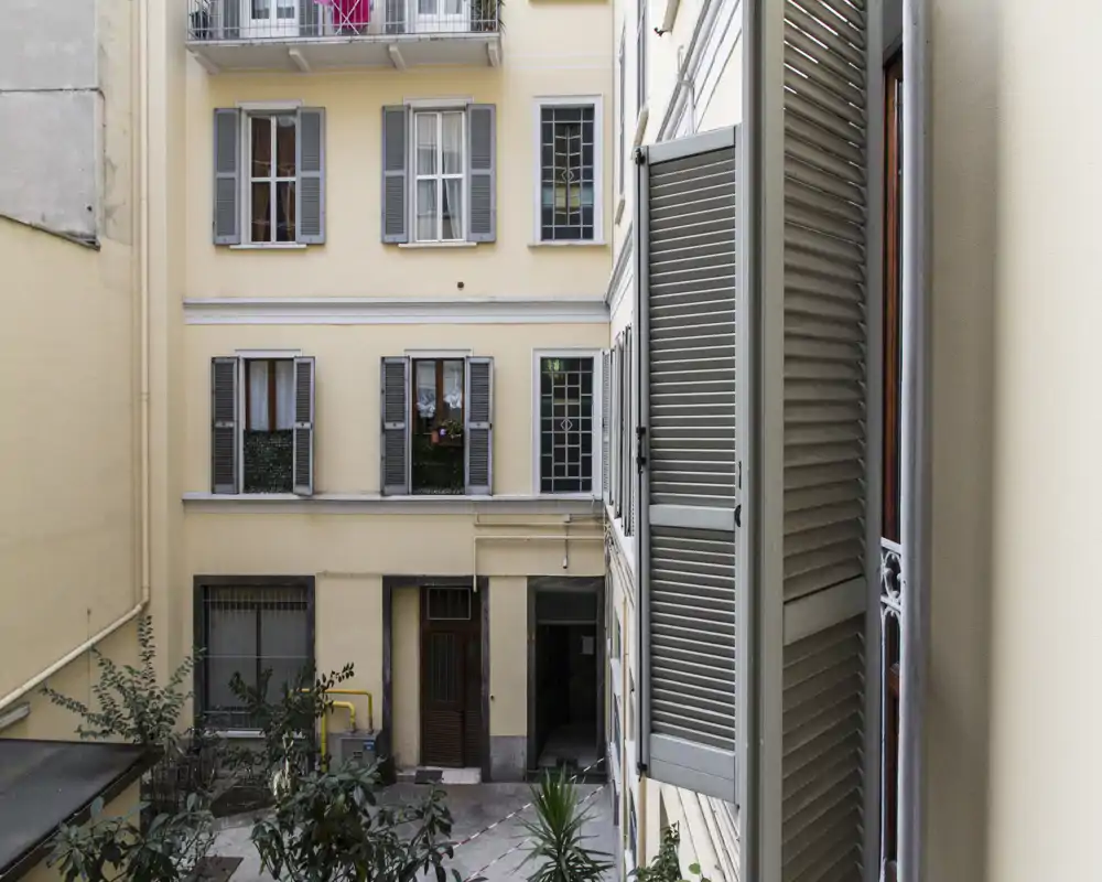 Vue sur une cour intérieure calme avec volets classiques et plantes en pot ; idéale pour une annonce d'appartement en ville mettant en valeur le patio intérieur.