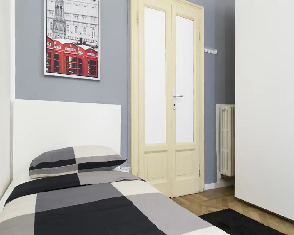 Chambre simple bien mise en scène avec tête de lit moderne, linge rayé et cadre mural; lumineuse, soignée et adaptée aux annonces locatives.