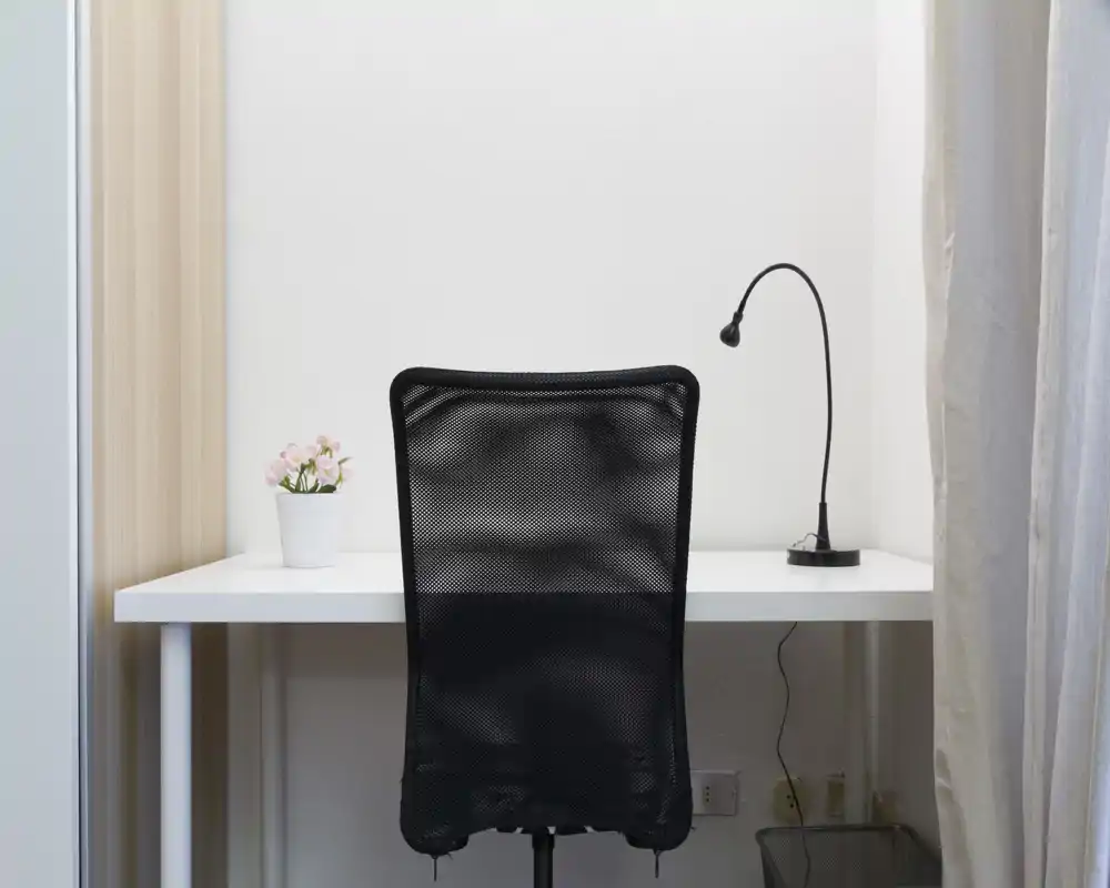 Espace de travail lumineux et minimaliste avec bureau blanc, chaise de bureau en maille noire, lampe flexible et petite plante en pot — propre, moderne et bien éclairé.