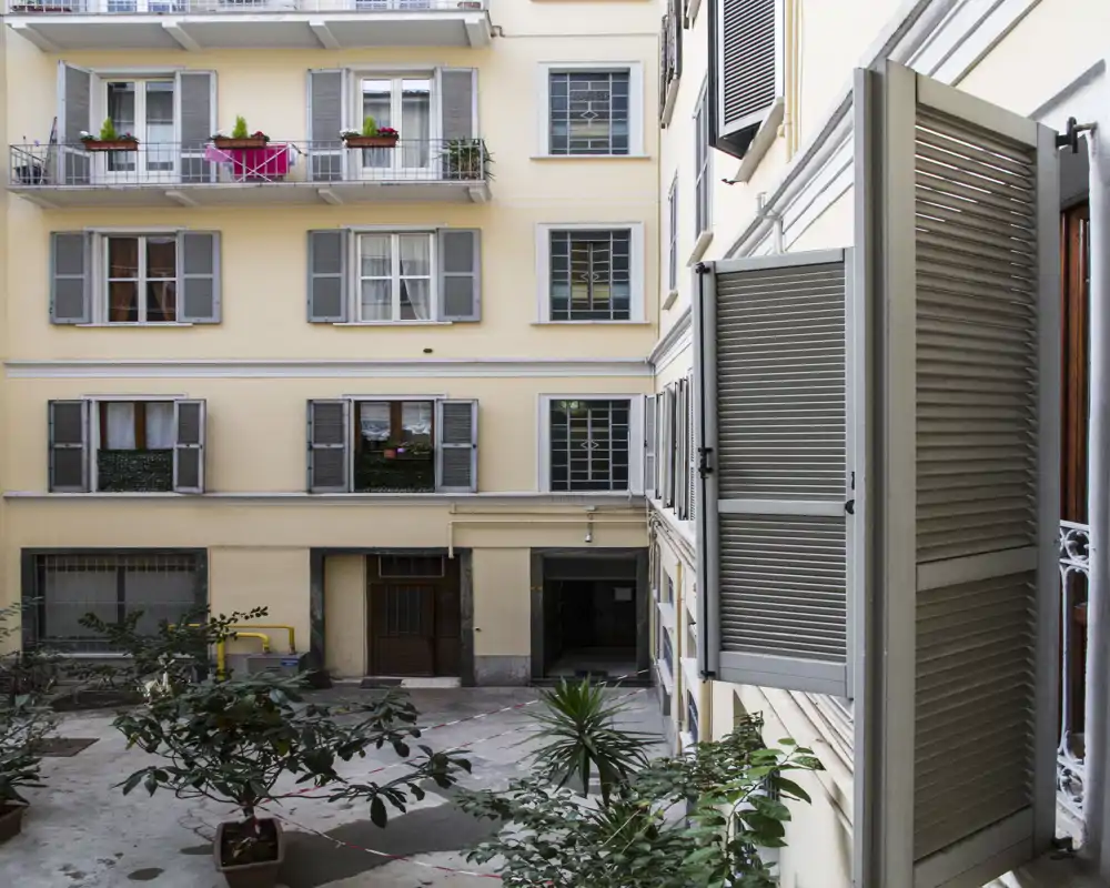 Vue sur une cour intérieure prise depuis un balcon, avec des plantes en pot et les fenêtres des appartements alentour.