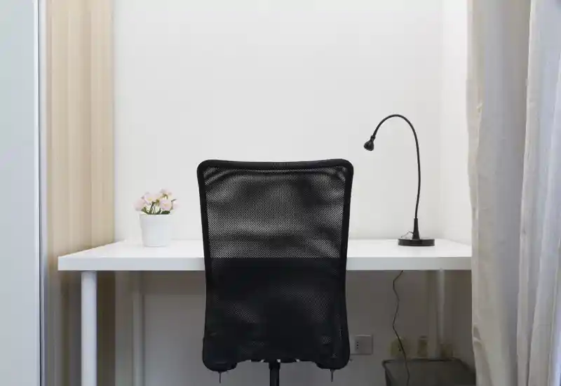 Angolo di lavoro luminoso e minimale con scrivania bianca, sedia da ufficio in rete nera, lampada flessibile e una piccola pianta in vaso — pulito, moderno e ben illuminato.