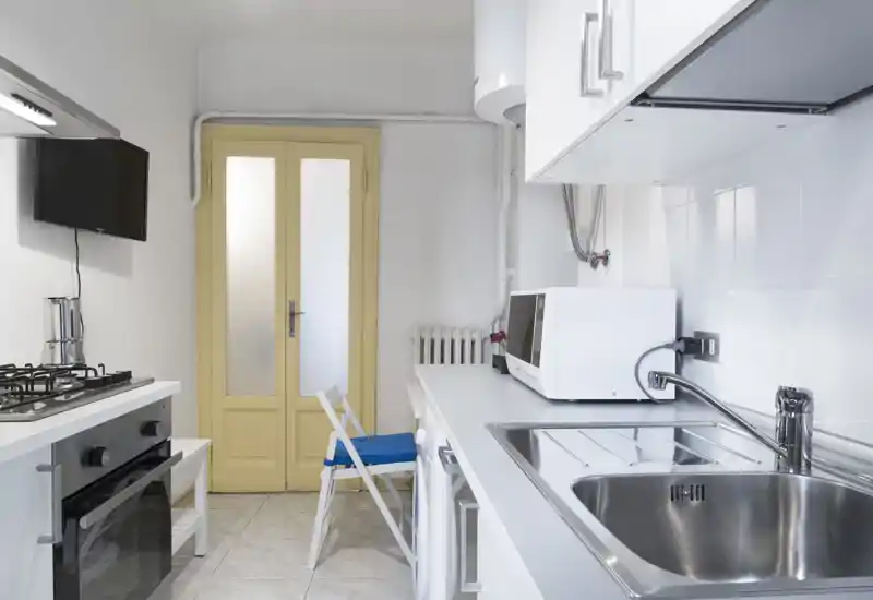 Bright, compact modern kitchen with stainless sink, gas stove, microwave and a small seating area; clean white finishes and efficient layout ideal for short-term rentals.