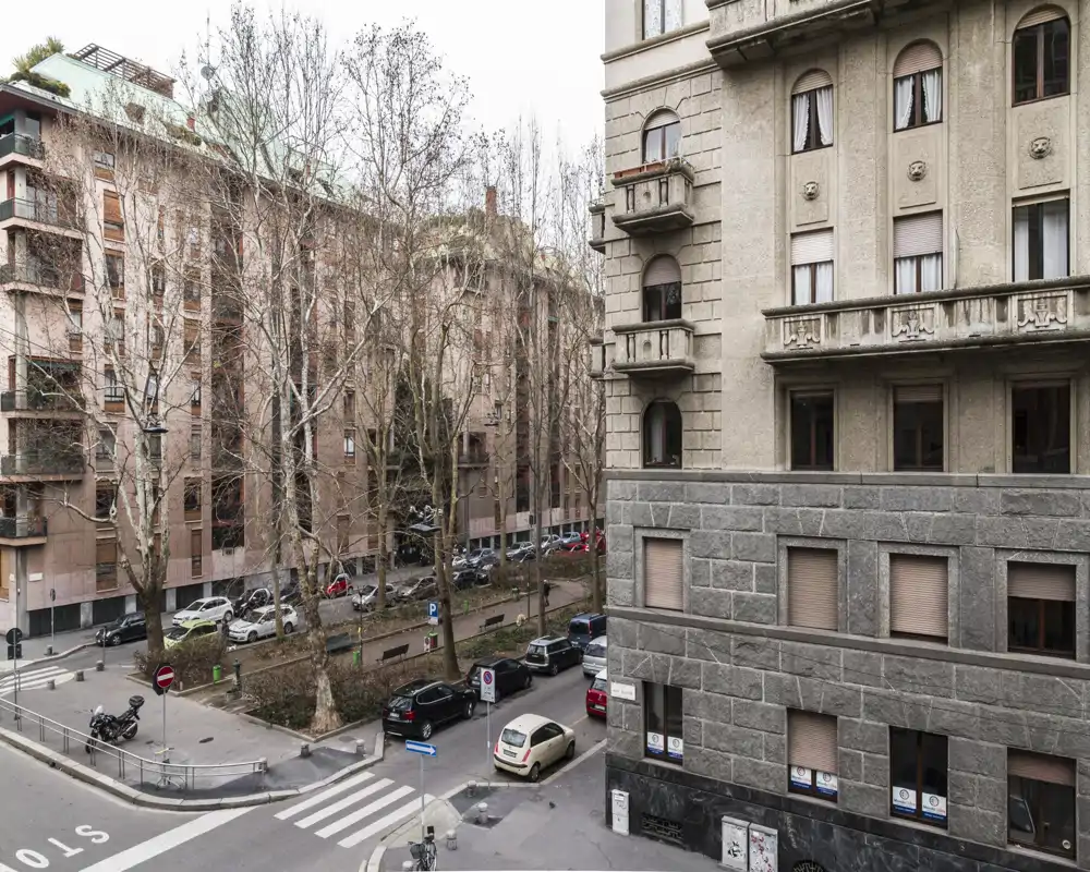 Urban street and building view from a window/balcony showing parked cars, trees and adjacent architecture — useful to showcase location and neighborhood.