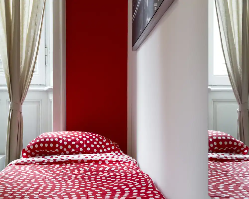 Bright, modern bedroom corner with a polka-dot red duvet and natural window light, offering a cozy, colorful single bed setup.