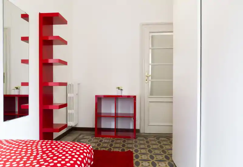 Bright, modern bedroom corner with a red polka-dot bedspread, matching red shelving and a small cubed storage unit on patterned tile flooring.