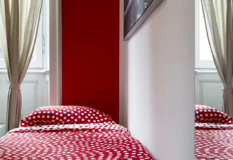 Bright, modern bedroom corner with a polka-dot red duvet and natural window light, offering a cozy, colorful single bed setup.