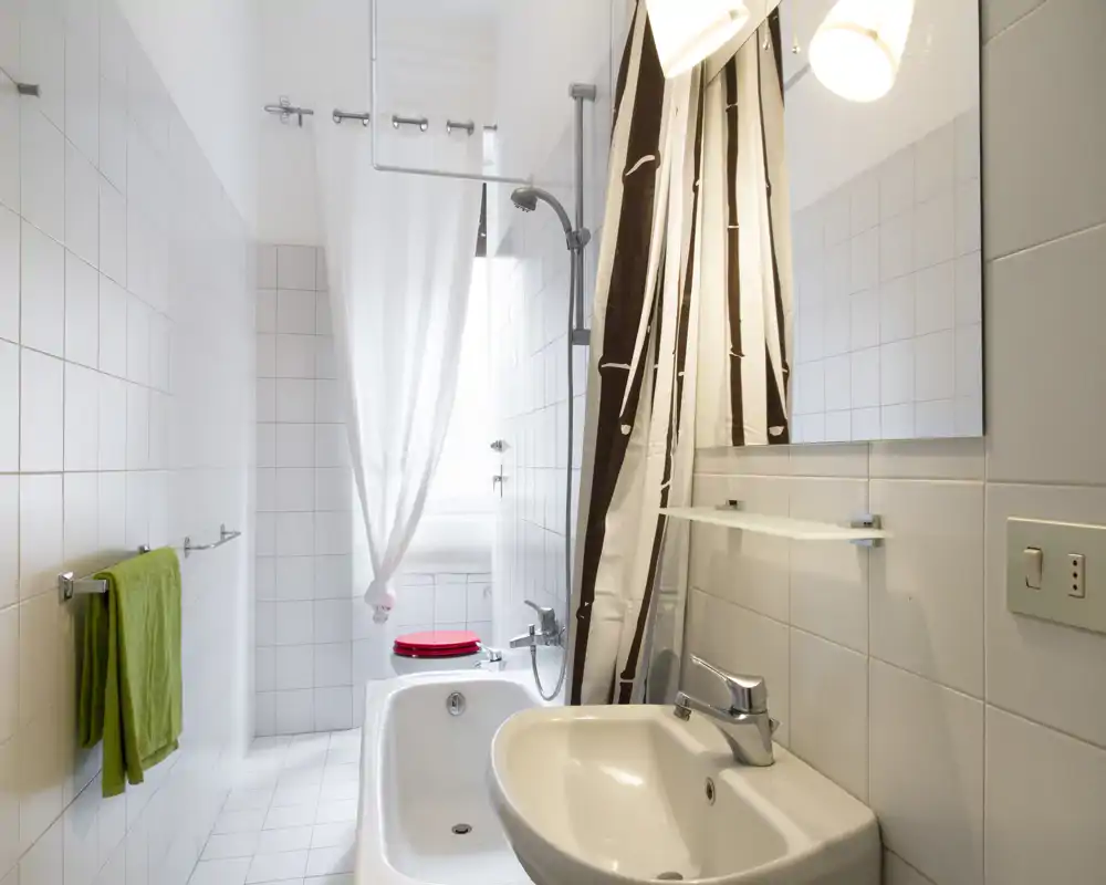 Bright, well-lit bathroom with a bathtub, shower curtain, sink and mirror; white tiles create a clean, minimalist look.