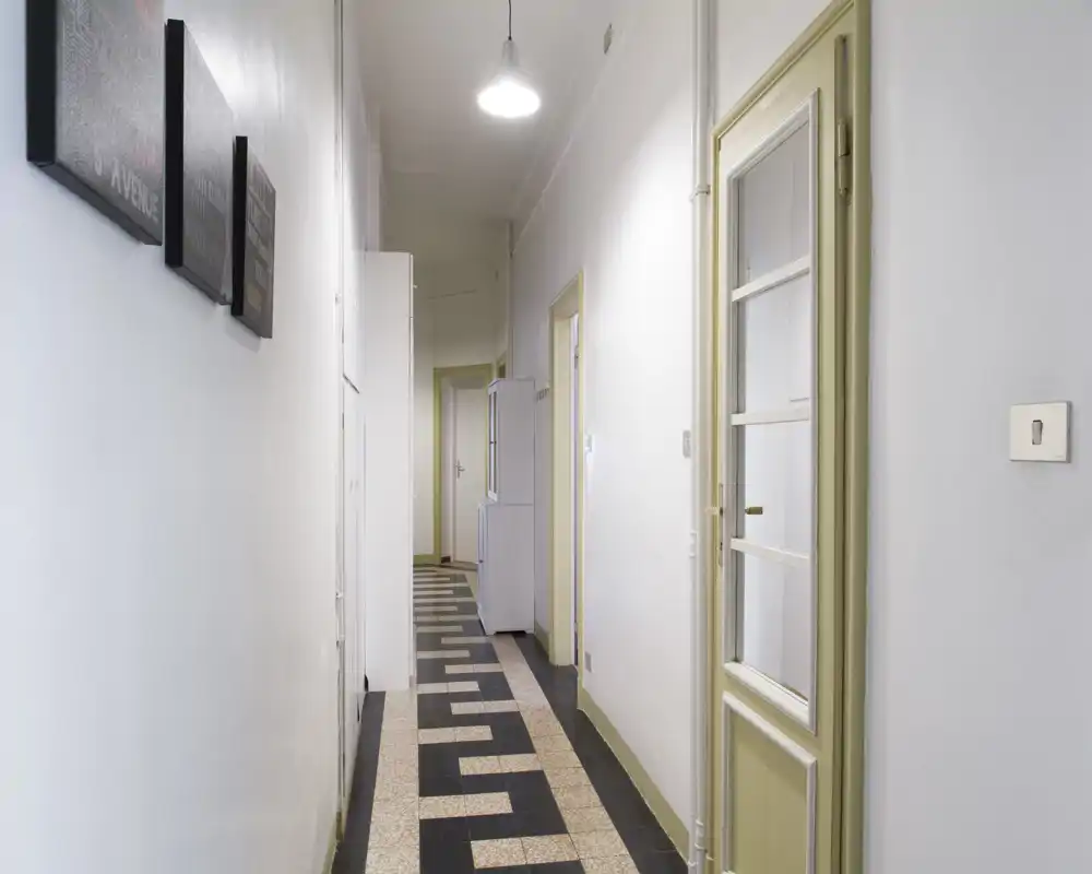 Bright, narrow hallway with patterned tile floor, white walls and multiple doors — an entrance corridor leading to inner rooms.