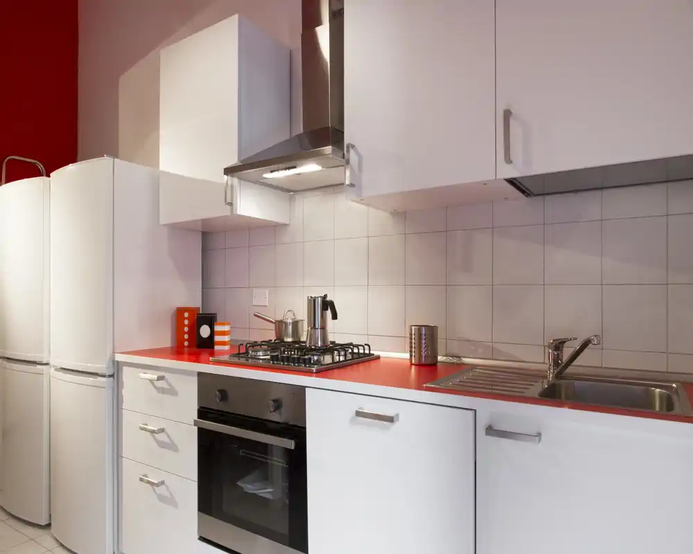 Modern, compact kitchen with a red countertop, gas hob, built-in oven and a stainless sink. Bright, clean design ideal for a small apartment.