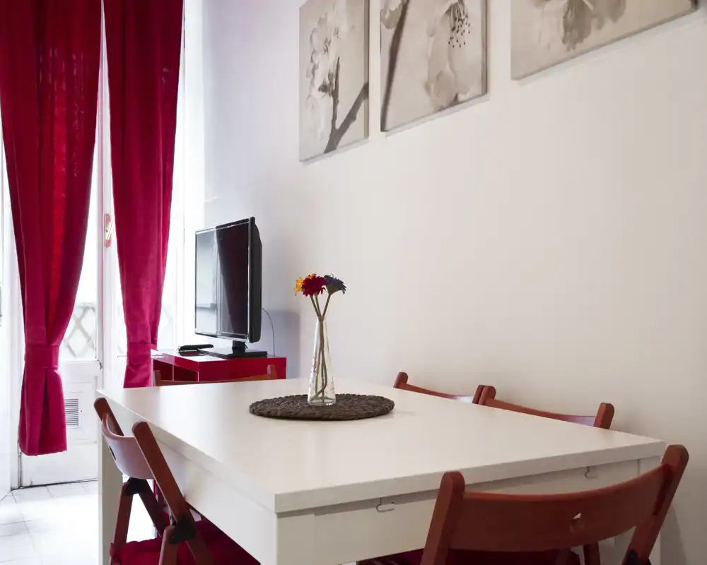 Bright, modern dining area with a white table, red folding chairs and a small vase centerpiece by a light-filled door.