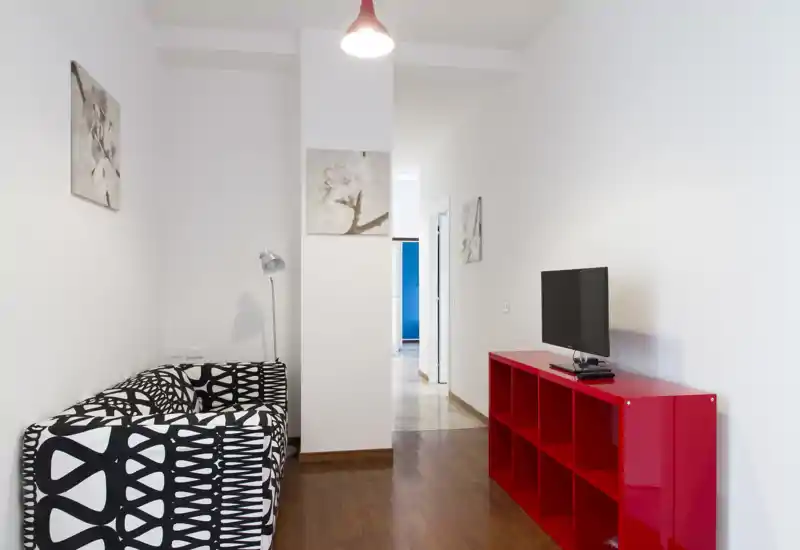 Small modern living area with a patterned black-and-white sofa, a red low shelving unit with TV, simple wall art and bright, clean lighting.