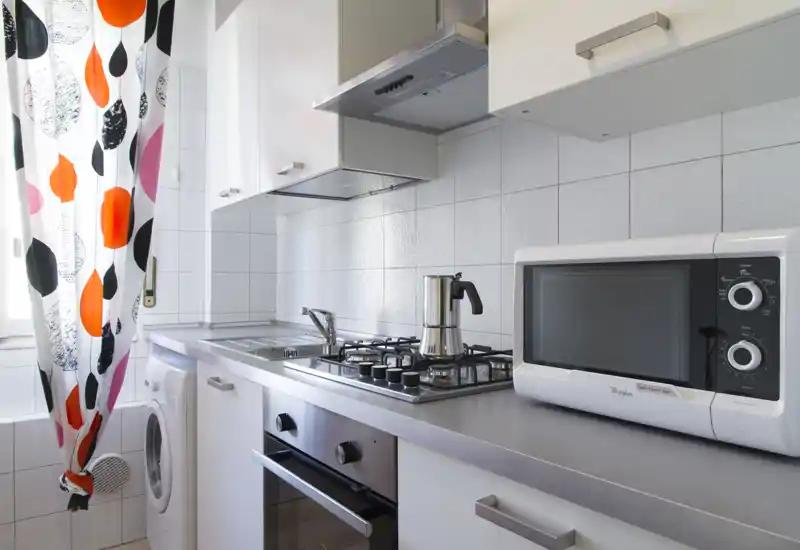 Bright, modern galley kitchen with stainless gas hob, built-in oven, microwave and a colorful curtain by the window — tidy and well lit.