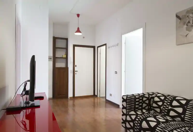 Bright, modern living area with a patterned sofa, wall-mounted TV on a glossy red console and wooden floors; clean, minimal styling suitable for rental photos.