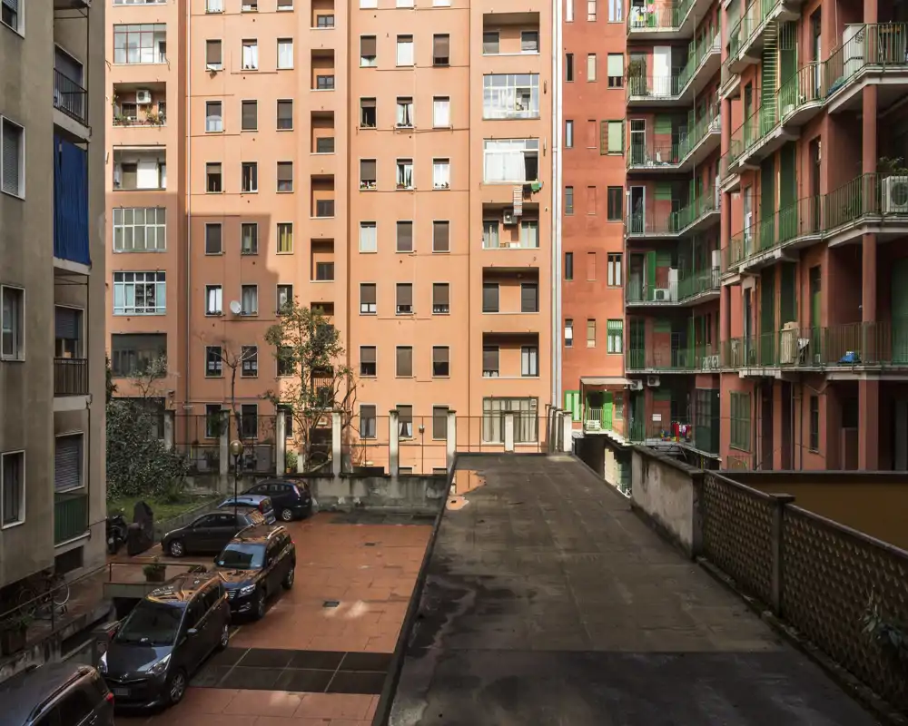 Inner courtyard view of an apartment block with parked cars, terracotta paving and multi-story façades — good for showing building exterior and shared parking space.