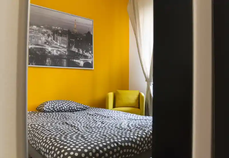 Camera da letto luminosa e ben curata con piumone a pois su un grande letto, parete gialla vivace e poltrona coordinata vicino alla finestra che crea un ambiente accogliente.