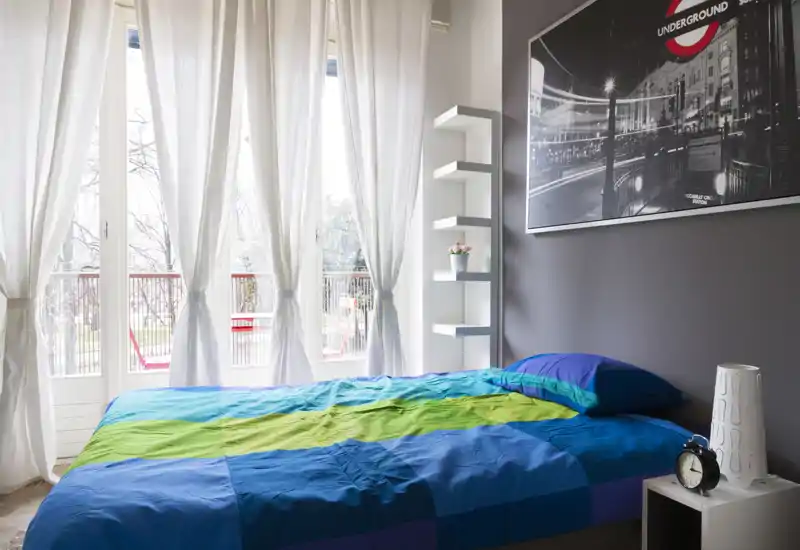 Camera da letto luminosa e moderna con grandi finestre e biancheria colorata; luce naturale morbida e arredo essenziale e curato.