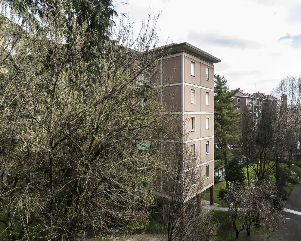 Vista de los exteriores del edificio con árboles grandes, senderos y bloques vecinos; agradable patio ajardinado visible desde un piso alto.