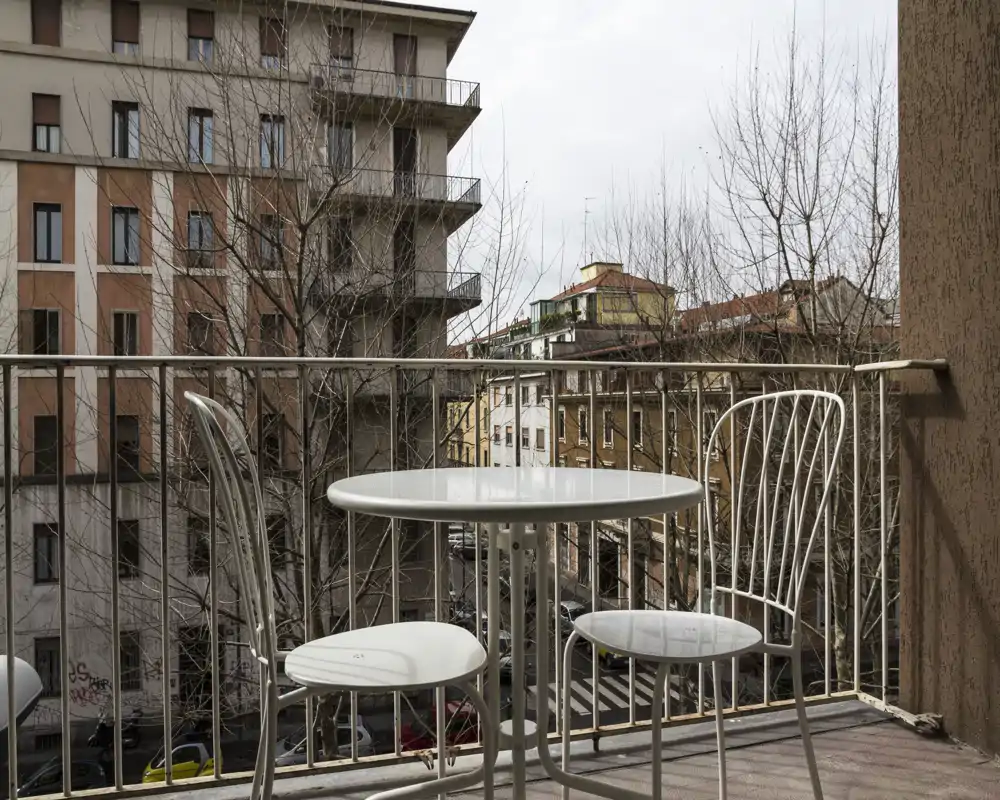 Balcón soleado con una mesa redonda pequeña y dos sillas de metal con vistas a la calle — ideal para el café de la mañana o un momento al aire libre.