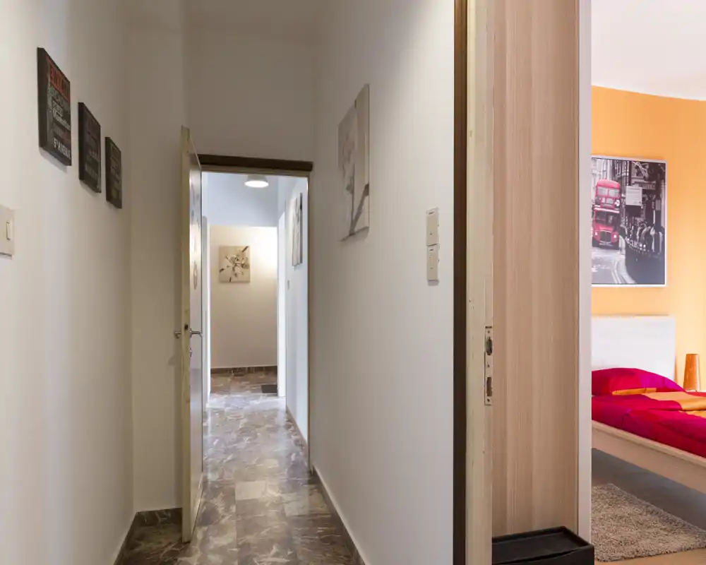Pasillo luminoso y estrecho con suelo de baldosas y puertas abiertas hacia otras habitaciones; decoración de pared sencilla y líneas limpias que crean un espacio de entrada neutro.