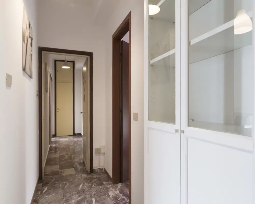 Entrada bien iluminada con suelo efecto mármol, paredes blancas y armario empotrado con puertas de vidrio — pasillo limpio y acogedor hacia las estancias interiores.