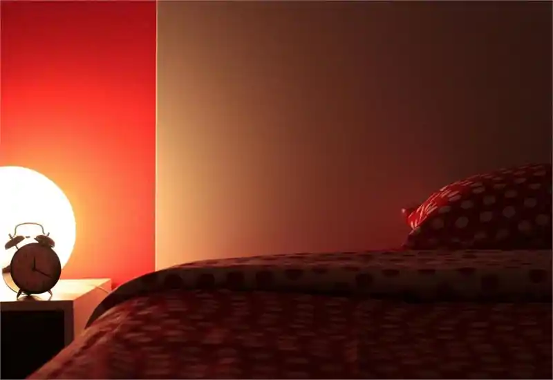 Angolo di camera da letto caldo e accogliente con biancheria a pois, una lampada da comodino luminosa e una sveglia classica che creano un'atmosfera serale invitante.