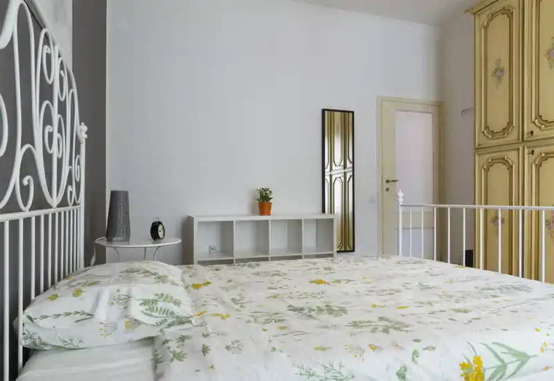 Dormitorio luminoso y bien cuidado con cabecero de hierro decorativo, edredón floral y un gran armario; la cama domina el primer plano y la habitación resulta limpia y acogedora.