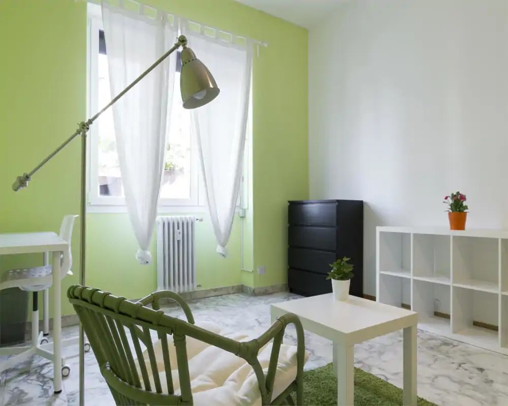 Area giorno luminosa e moderna con parete verde chiaro, poltrona confortevole, tavolino e scaffalatura — ben illuminata e arredata con gusto per un soggiorno rilassante.