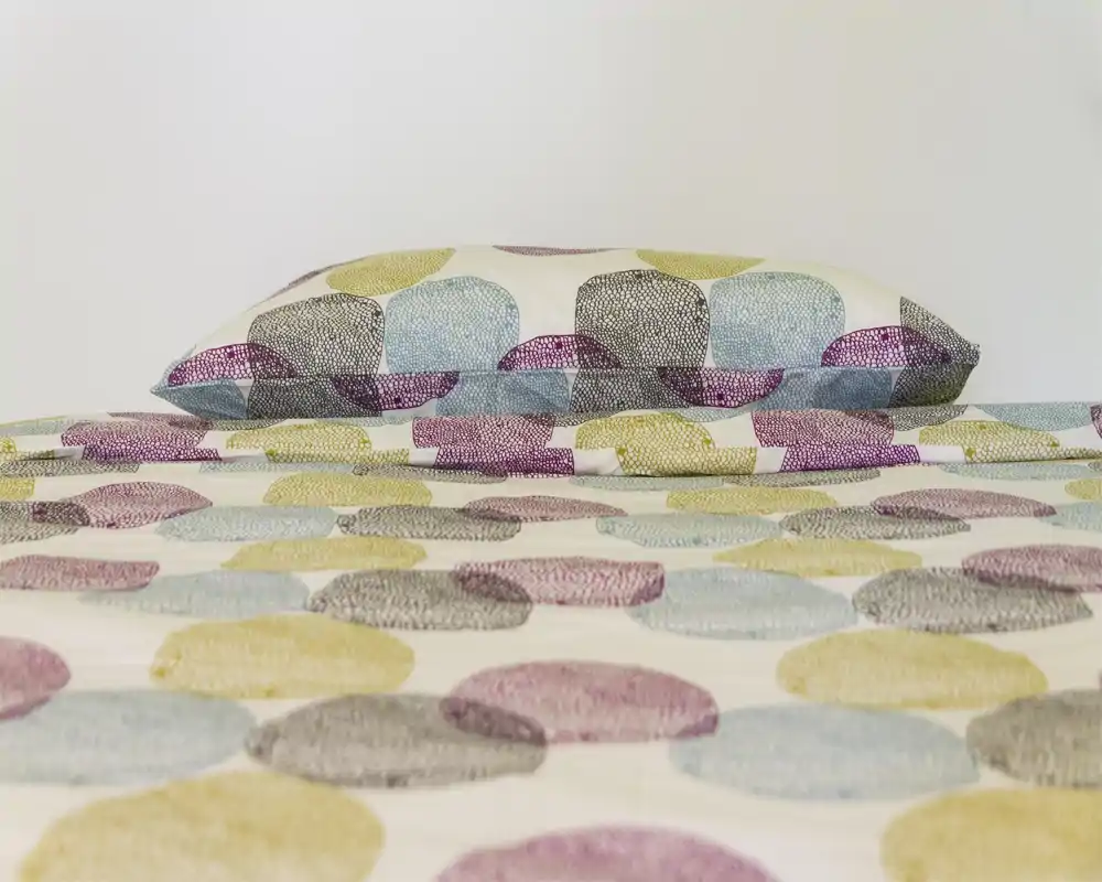 Scatto luminoso e ravvicinato di una camera da letto che mostra un letto ben rifatto con copripiumino a fantasia e cuscino abbinato; lo sfondo minimalista mette in risalto la biancheria.