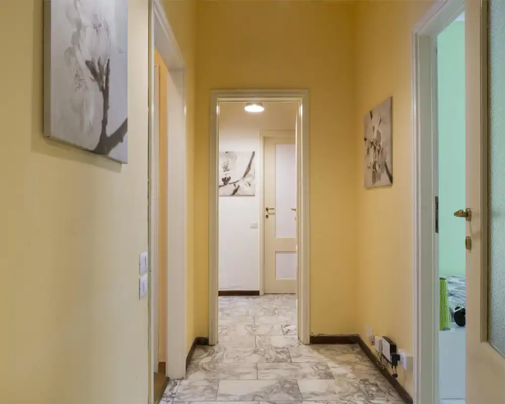 Pasillo interior luminoso con paredes amarillas cálidas, suelo de efecto mármol y varias puertas que conducen a las habitaciones — apto como entrada o espacio de paso.