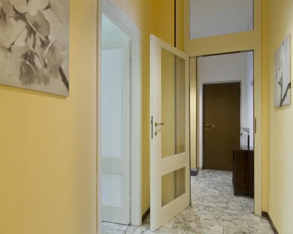 Vestíbulo de entrada luminoso con paredes amarillas, suelo tipo mármol y puerta interior blanca abierta que conduce a otras estancias — imagen adecuada para mostrar la zona de entrada.