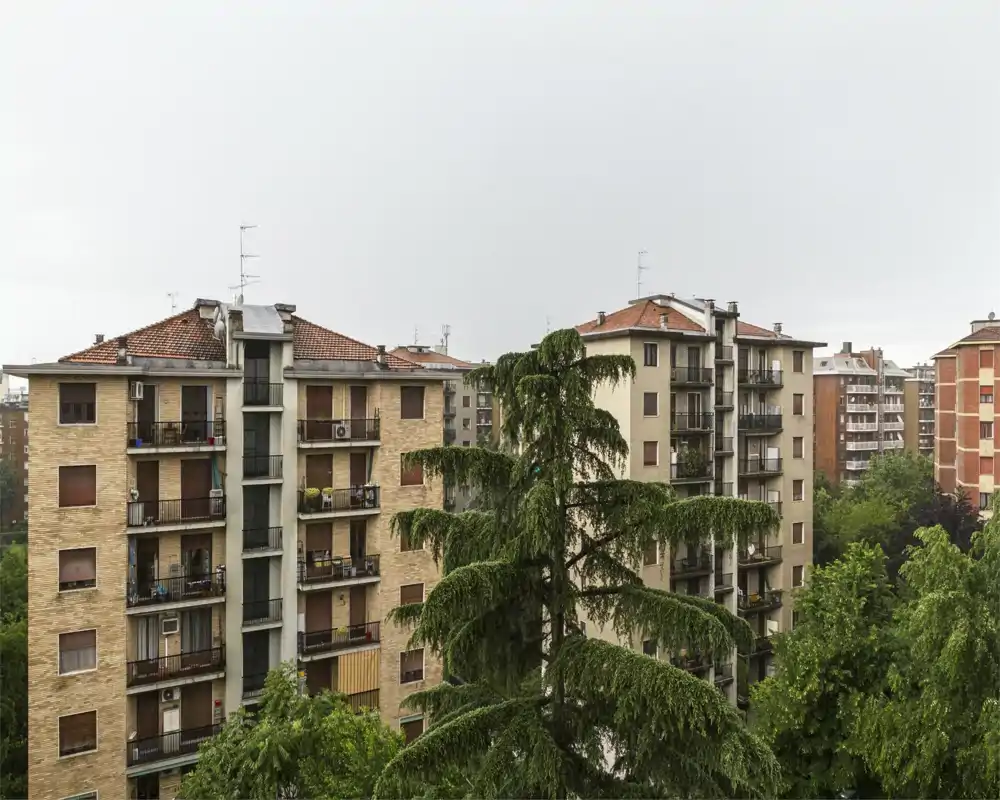 Vista exterior a edificios residenciales con árboles frondosos en primer plano, tomada en un día nublado.