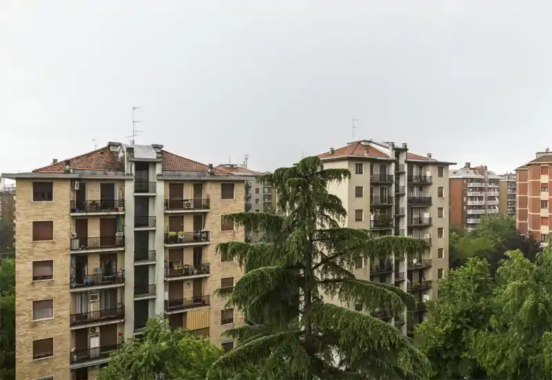 Vista exterior a edificios residenciales con árboles frondosos en primer plano, tomada en un día nublado.