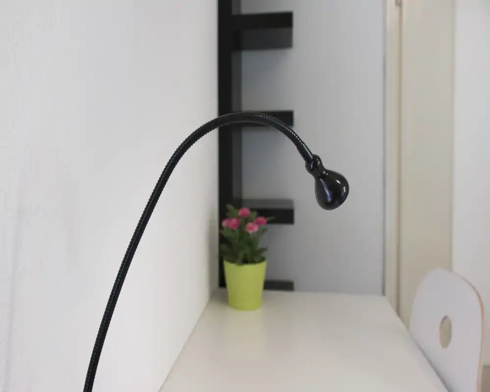 Rincón de escritorio minimalista con una lámpara negra flexible, una pequeña planta en maceta y una superficie blanca limpia — ideal para un espacio de trabajo compacto.