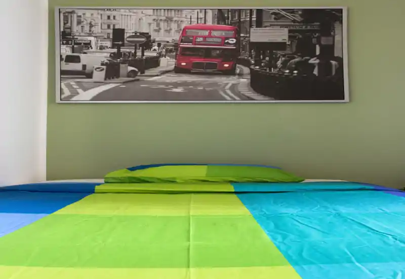 Dormitorio luminoso y colorido con una cama grande en primer plano y un cuadro de un autobús de Londres sobre la cabecera.