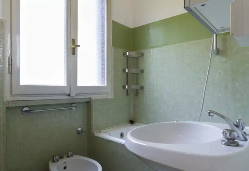 Bright bathroom with green mosaic tiles, bathtub, wall-mounted showerhead and a white sink—clean, well-lit space suitable for a rental listing.