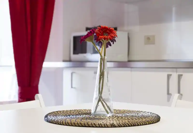 Bright, modern kitchenette with a vase of flowers on a round white table and a microwave and countertop in the background.