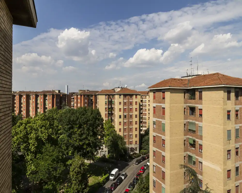 Vista esterna soleggiata da un balcone su palazzi residenziali, strade alberate e cielo azzurro con nuvole — perfetta per mostrare il quartiere e gli spazi esterni dell’immobile.