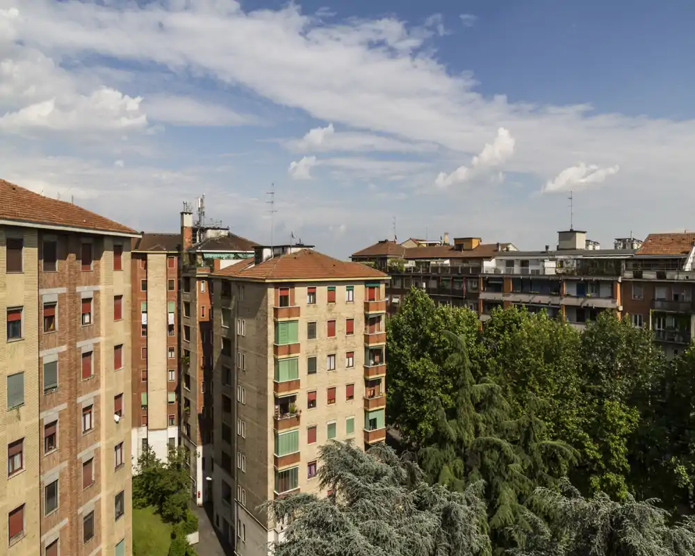 Veduta esterna urbana con edifici condominiali, chiome degli alberi e cielo azzurro — perfetta per illustrare la vista da un balcone o terrazzo.